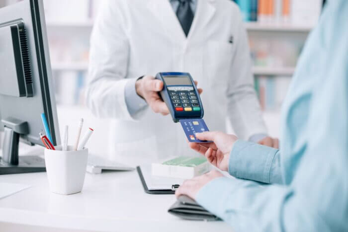 Healthcare professional holding payment terminal while patient uses card at dental office desk.