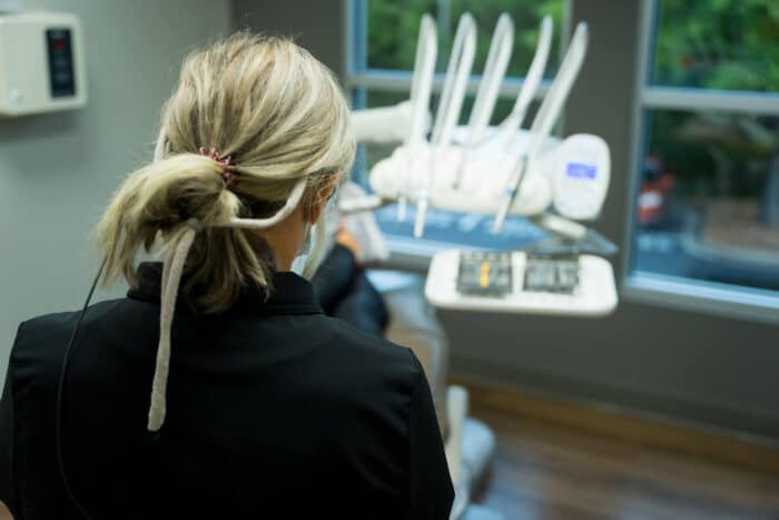 Dental professional examining equipment in modern clinical operatory with blue instruments and window view.