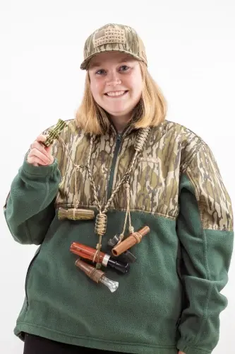Smiling young woman in camouflage hunting gear holding shotgun shells.