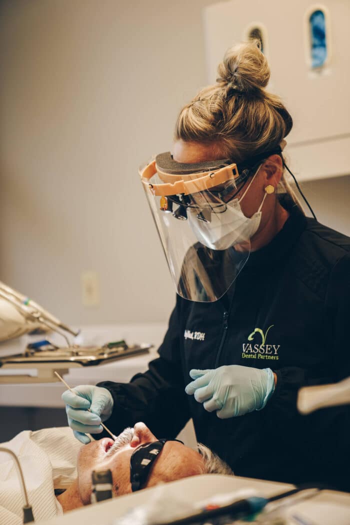 Dentist wearing protective gear performing dental procedure on patient in clinical setting.