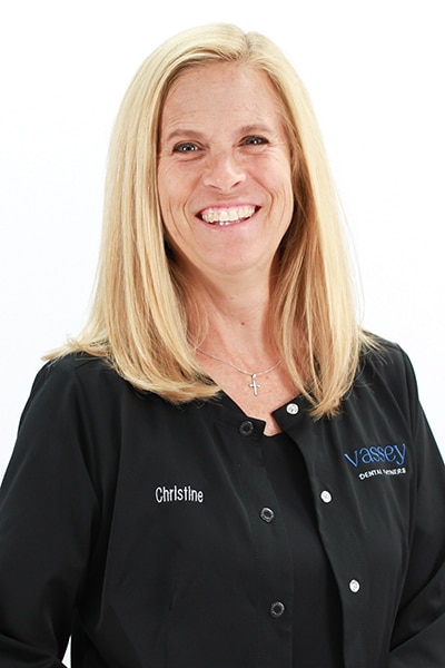 Professional headshot of blonde woman smiling in black Vassey Dental polo shirt against white background.