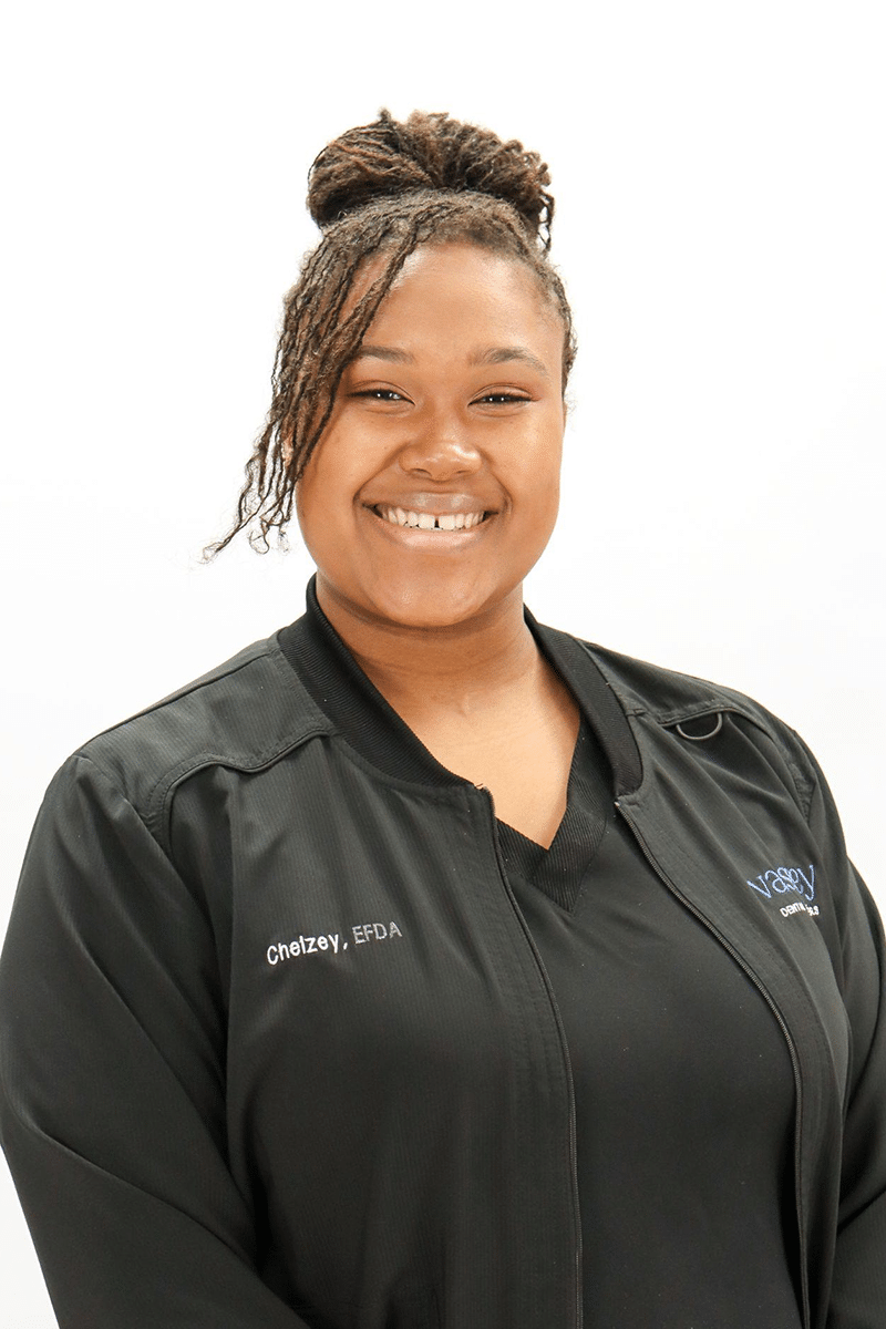 Professional headshot of smiling dental staff member wearing black Vassey Dental uniform against white background.