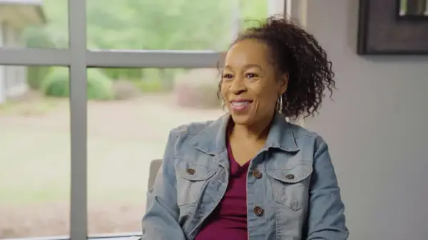 Woman in denim jacket smiling near window in professional dental office setting.