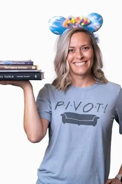 Smiling woman wearing Friends PIVOT shirt and Mickey ears holding books at Peachtree City dental practice.