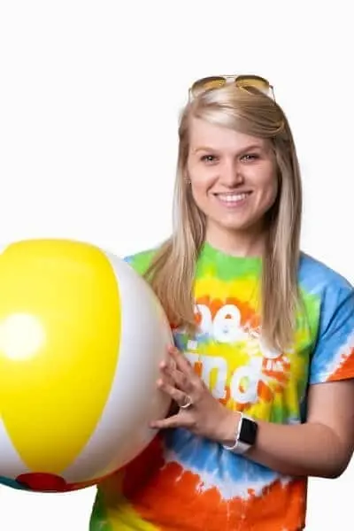 Smiling young woman holding a colorful beach ball wearing tie-dye shirt.