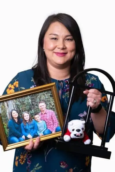 Dr. Michelle smiles while holding a family photo and headphones at her Peachtree City dental practice.
