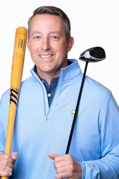 Male dentist holding a baseball bat and golf club, smiling at camera in professional blue shirt.