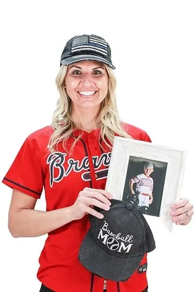 Woman in red Braves baseball jersey holding baseball mom hat and framed photo.