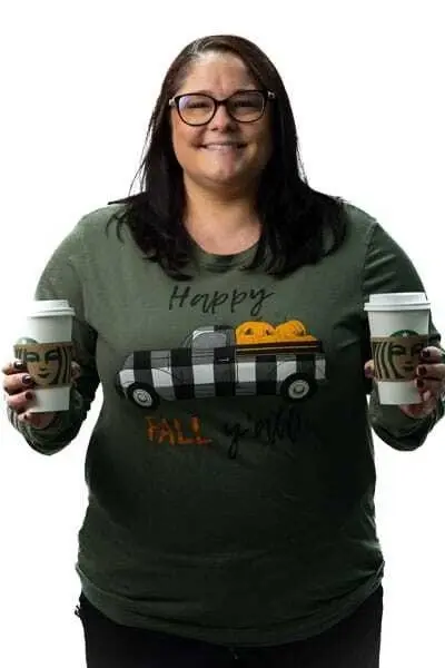 Smiling woman holding fall-themed coffee cups in a Happy Fall graphic t-shirt.